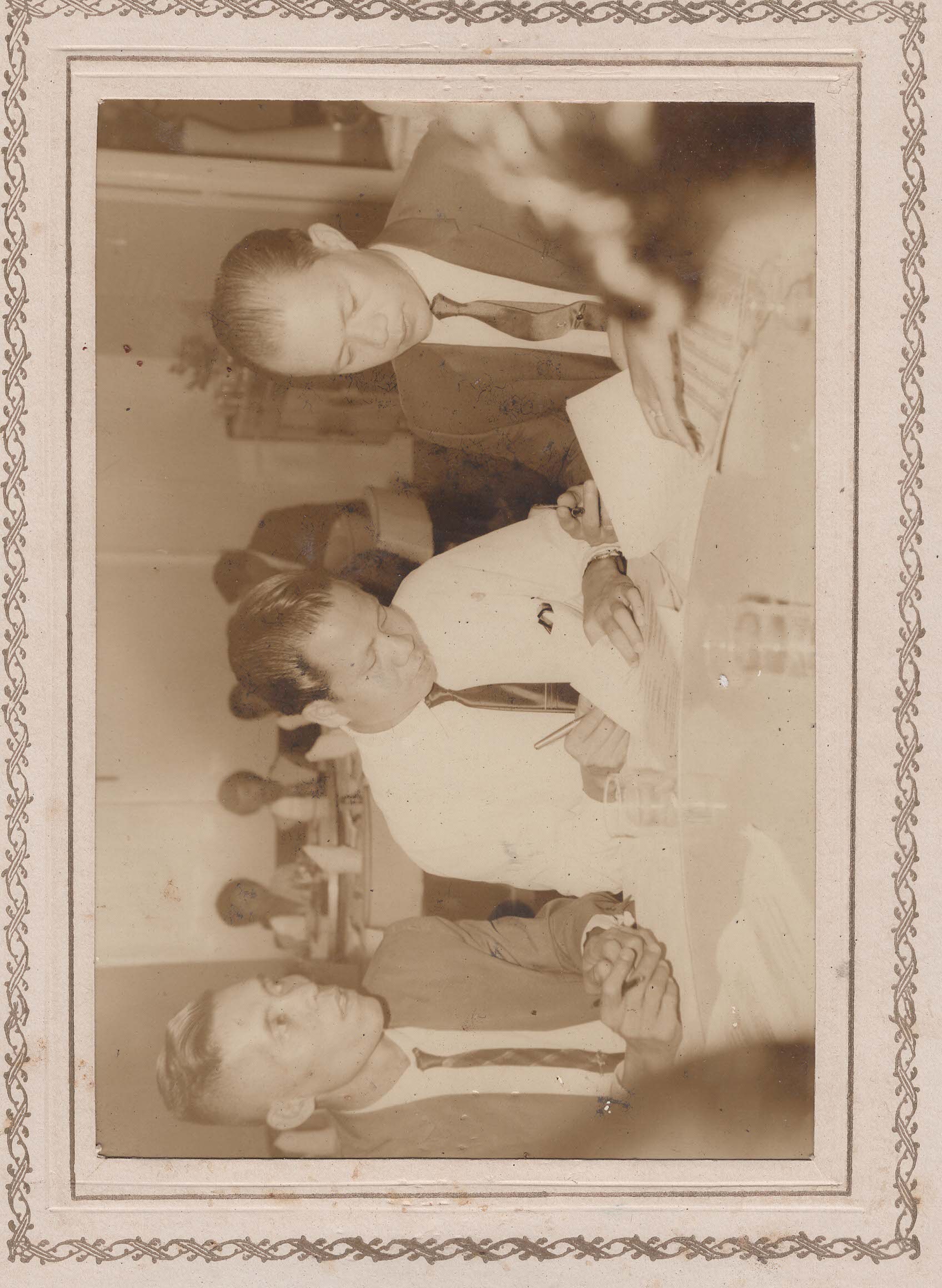 Three men at a restaurant table, one signing a document