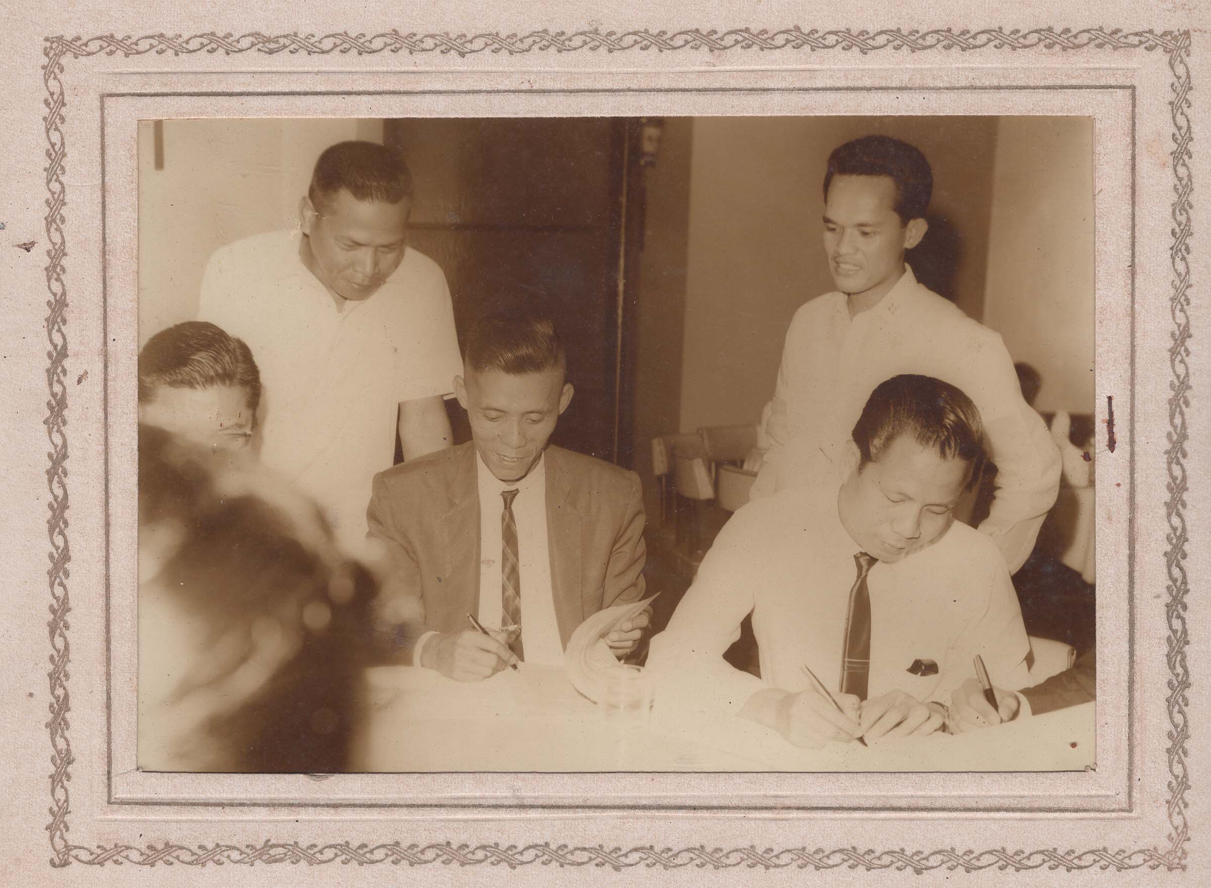 Four men gathered around a table signing documents